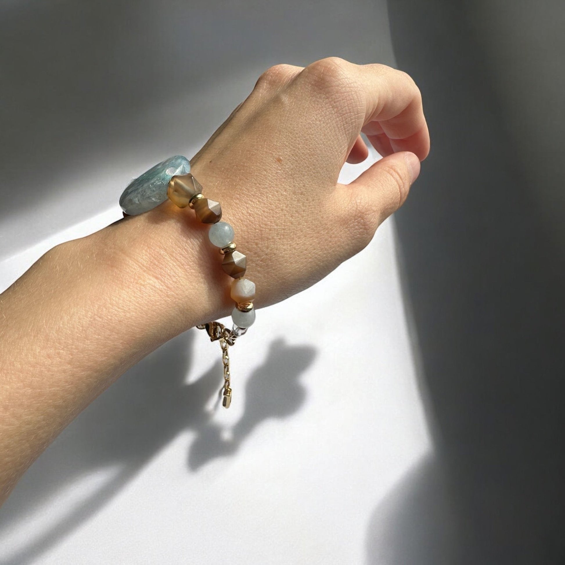 An aquamarine and agate crystal bracelet with gold plating on a hand
