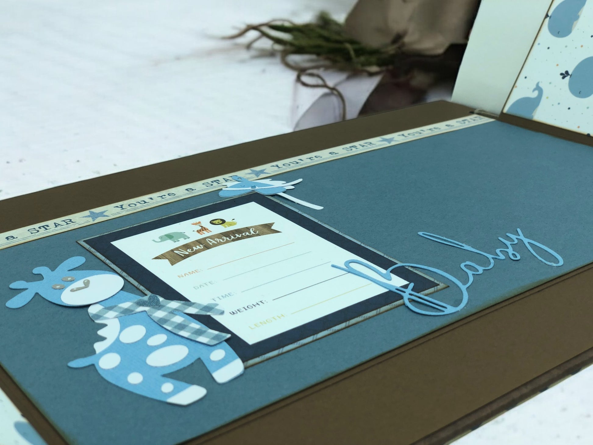 Customisable blue baby album A4 with ribbons, wooden cut-outs, handmade animals and info card—artisan photo book for baby showers and new parents.