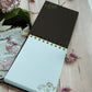Flat lay of A6 cockatoo notebook with golden spiral binding, designer paper cover and ribbon bow—handmade journal for everyday notes and sketches.