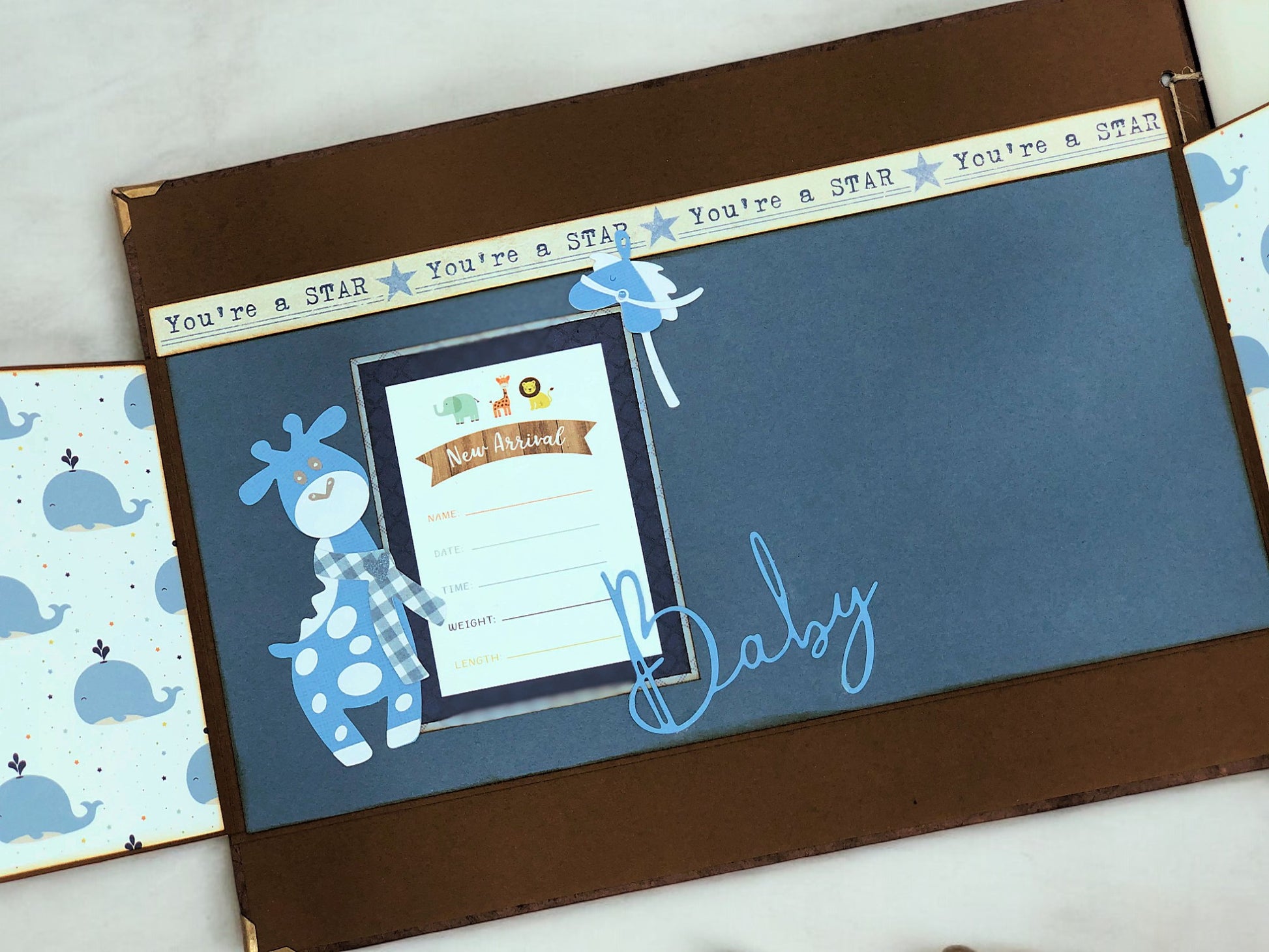 Flat lay of handmade A4 blue baby photo album with Maja design paper, bronze details and ribbon accents—customisable photo book for baby memories.