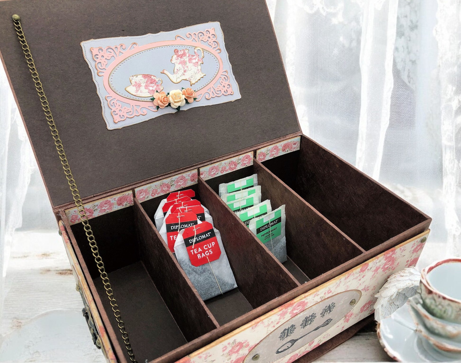 Flat lay of vintage shabby chic pink rose tea organiser chest with bronze metal accessories and Maja design papers—artisan handmade tea storage box.